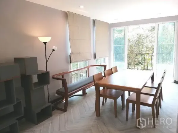 Townhouse for rent or sale in Suan Luang, Bangkok - Windowed dining room with wooden table and chairs opening to greenery.