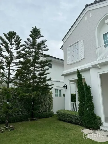 Detached House for rent or sale in Bang Phli, Samut Prakan - Side garden with tall pine trees beside the white facade.