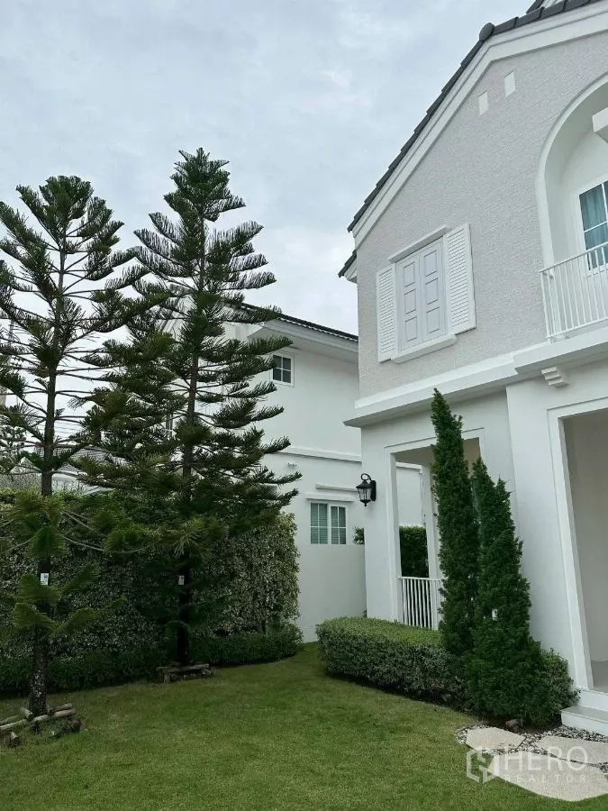 Detached House for rent or sale in Bang Phli, Samut Prakan - Side garden with tall pine trees beside the white facade.
