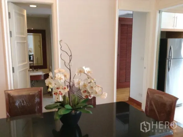 公寓 出租或出售在Watthana, Bangkok - 餐区设黑色亮面餐桌与兰花摆件，连通厨房与浴室。