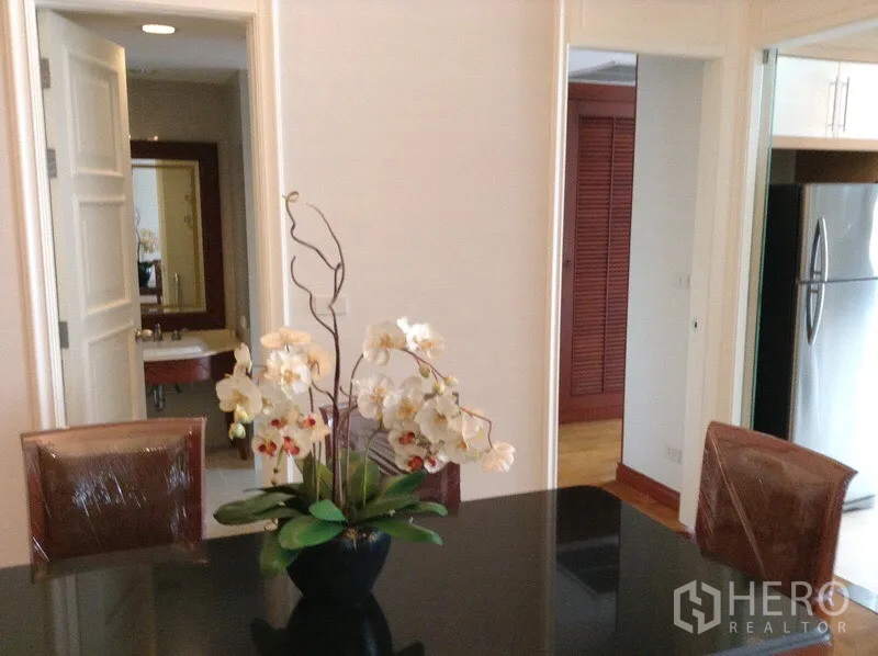 公寓 出租或出售在Watthana, Bangkok - 餐区设黑色亮面餐桌与兰花摆件，连通厨房与浴室。