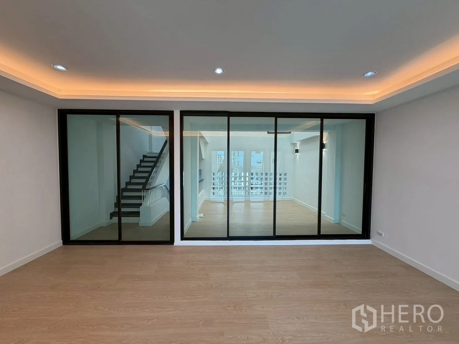 Townhouse for sale in Phra Khanong, Bangkok - Open room facing a wall of tinted sliding glass panels with stairs beyond.