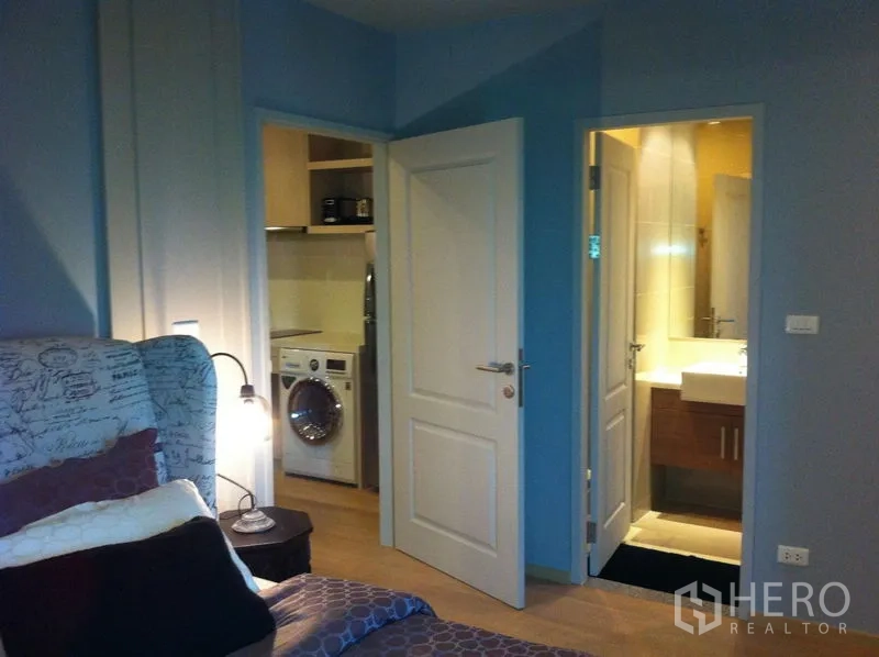 Condominium for rent in Bangkok - Bedroom corner showing doors to a modern bathroom and a laundry nook with washing machine.