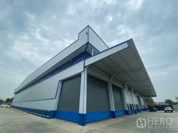 Warehouse for rent in Pathum Thani - Corner view of a new warehouse showing multiple roller shutters and a large covered loading dock.