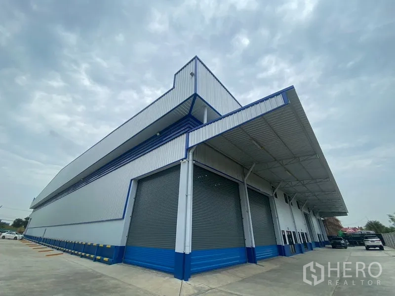 Warehouse for rent in Pathum Thani - Corner view of a new warehouse showing multiple roller shutters and a large covered loading dock.