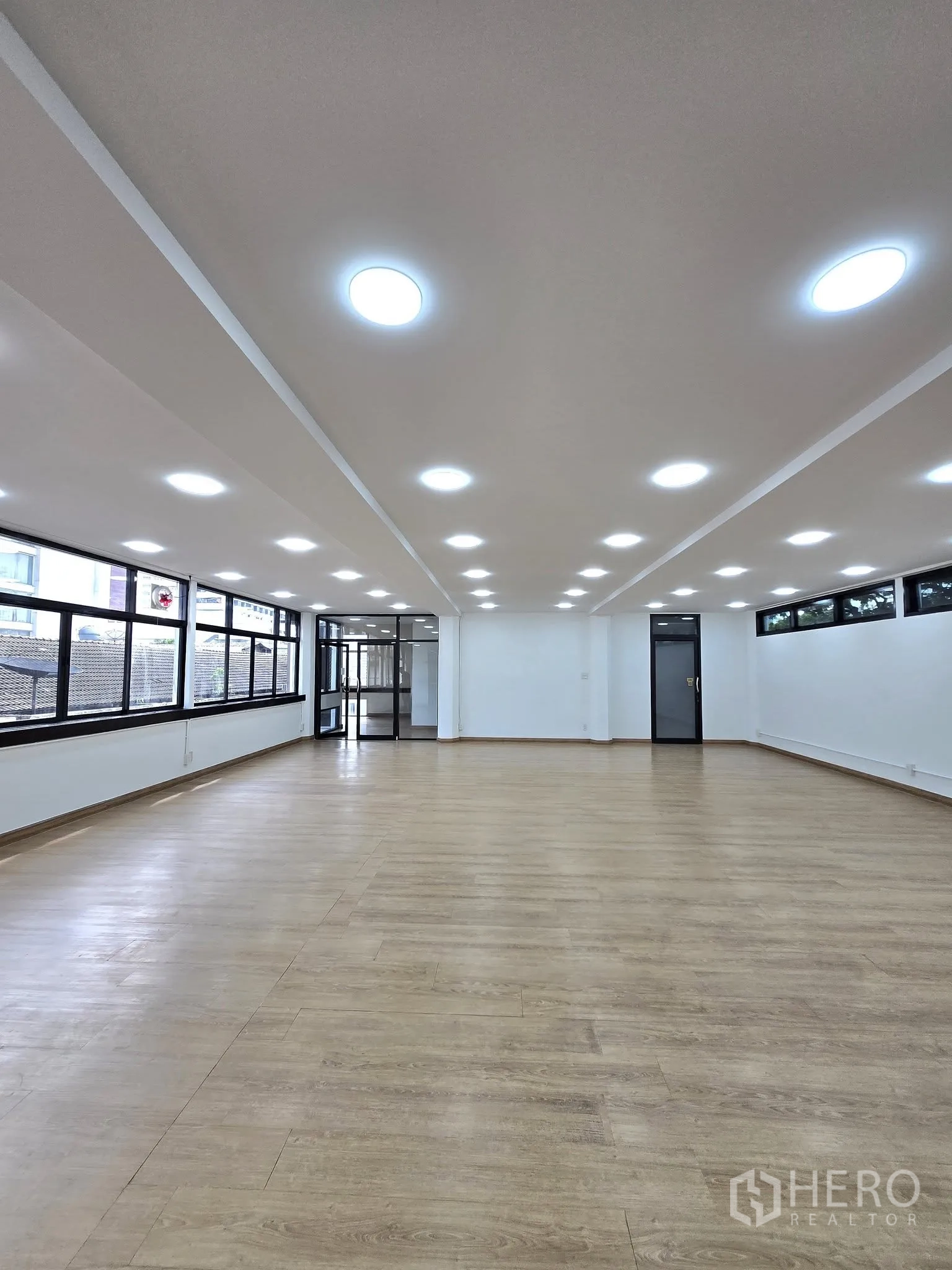 Office Space for rent in Khlong Toei, Bangkok - Long open workspace with LED lights, wood flooring, black-framed windows, and a glass entry.