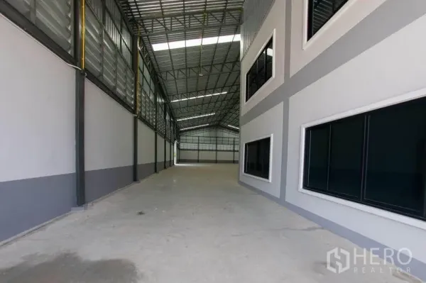 Warehouse for sale in Krathum Baen, Samut Sakhon - Covered loading lane with high roof and side windows along the warehouse wall.