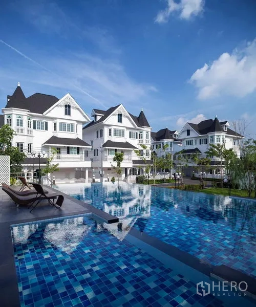 Townhouse for rent or sale in Mueang Samut Prakan, Samut Prakan - Communal swimming pool with deck chairs and white townhouses around.