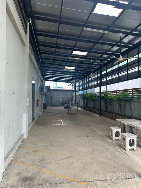 Warehouse for rent or sale in Lam Luk Ka, Pathum Thani - Deep covered side yard with concrete floor and benches for staging goods.