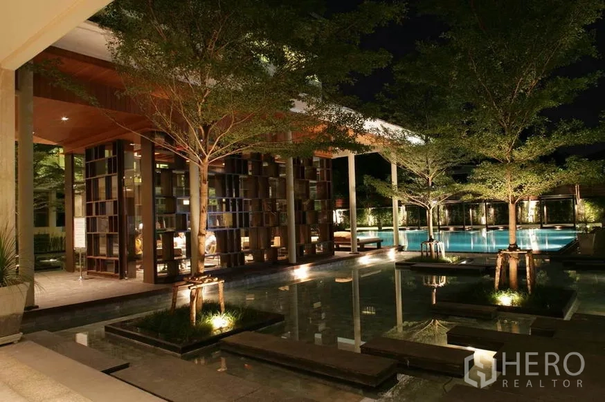 Condominium for sale in Khlong Toei, Bangkok - Night view of resort-style swimming pool with landscaped water features, trees and open-air pavilion.