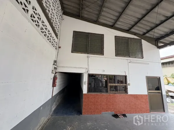 Warehouse for rent in Mueang Samut Prakan, Samut Prakan - Ground-floor office entrance with grilled windows, fire extinguisher and canopy beside the loading area.