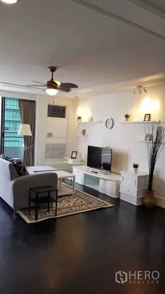 Condominium for rent in Khlong Toei, Bangkok - Lounge with ceiling fan, TV unit and wall shelves next to a large window.