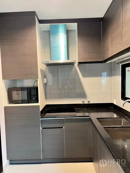 Townhouse for rent in Saphan Sung, Bangkok - Compact L-shaped kitchen with range hood, microwave and dark stone countertops.