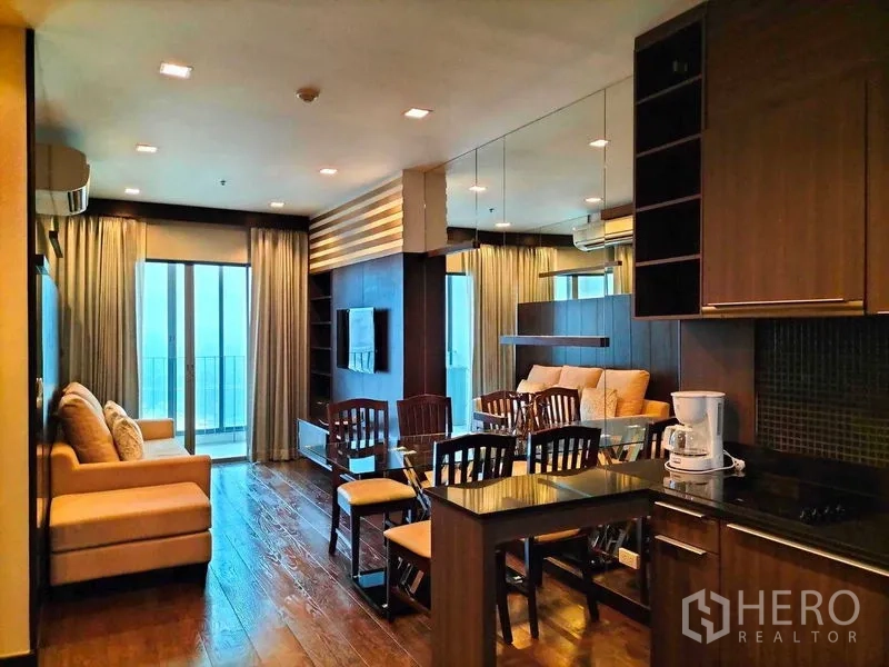 Condominium for rent in Ratchathewi, Bangkok - Open-plan living area with kitchen, mirror wall, dining table and access to balcony.