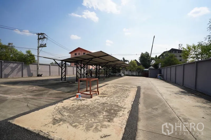 Factory for sale in Khlong Luang, Pathum Thani - Wide concrete yard with covered loading and parking bays inside a fenced compound.