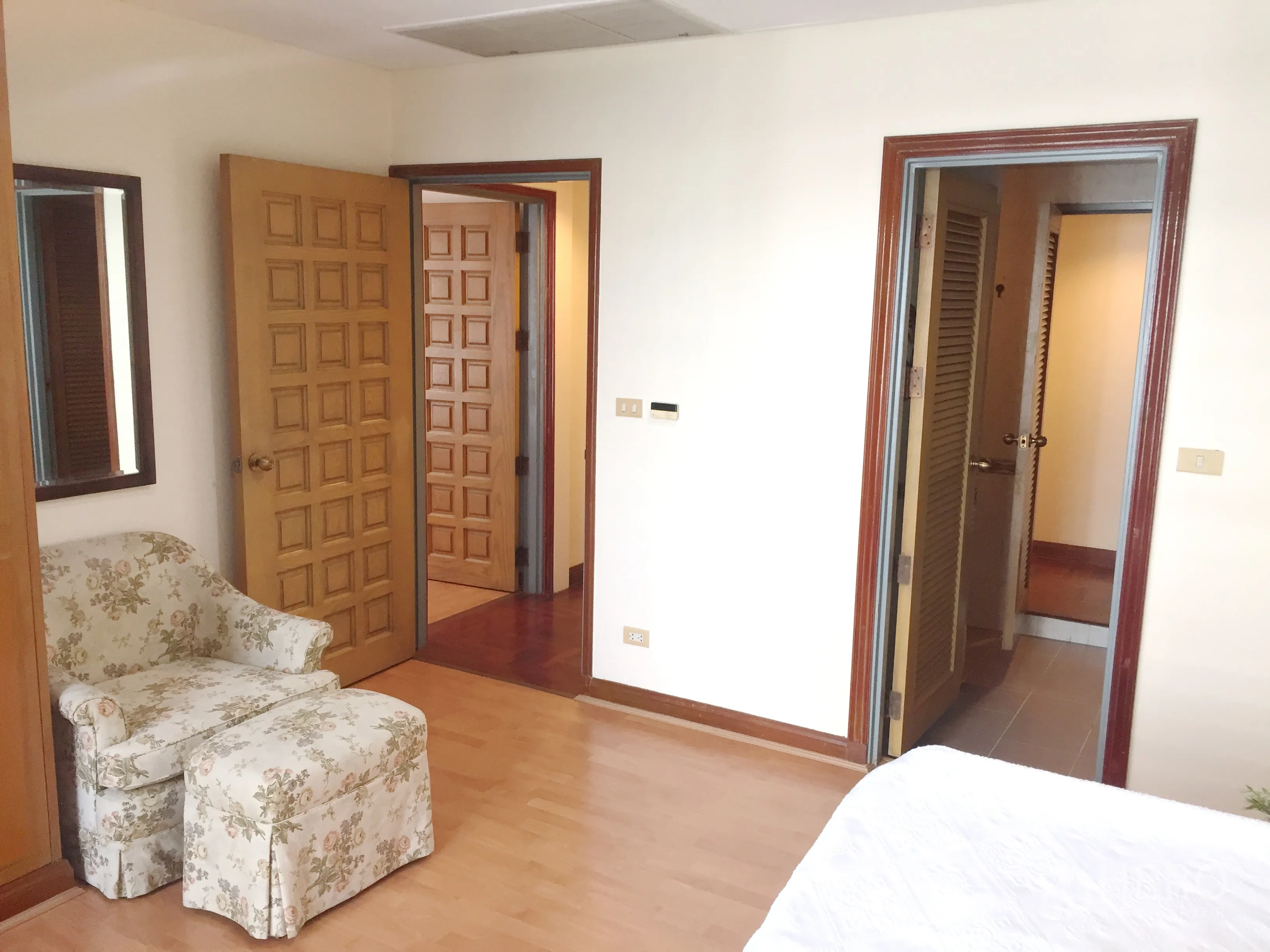 公寓 出租在Pathum Wan, Bangkok - 卧室一角，花纹单人沙发，木门，连接套内卫生间的通道