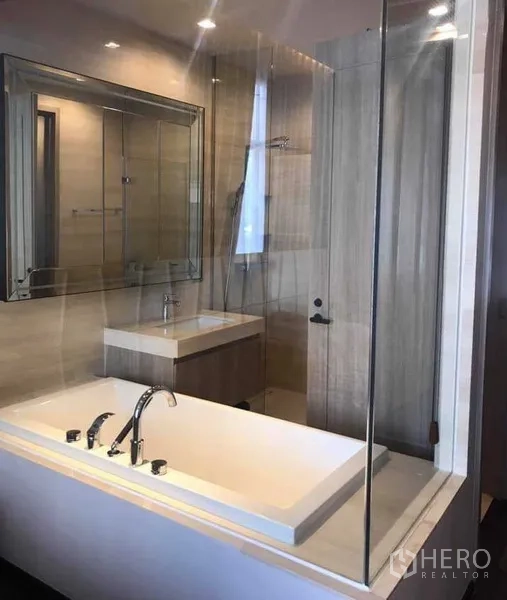 Condominium for rent or sale in Watthana, Bangkok - Modern bathroom with built-in bathtub, glass partition, vanity and wall mirror.
