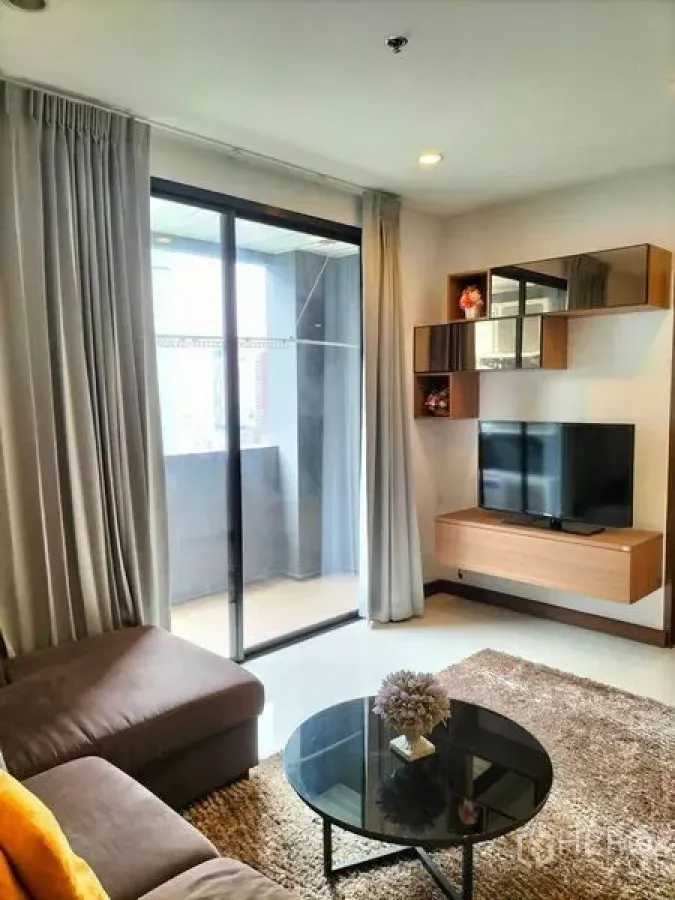 Condominium for rent in Watthana, Bangkok - Living area with TV wall unit and sliding glass door opening to the balcony.