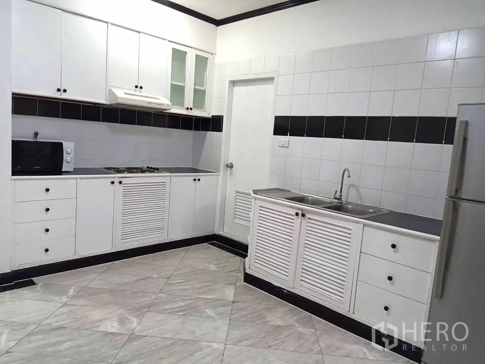 Condominium for rent in Watthana, Bangkok - Full kitchen with upper and lower white cabinetry, cooktop, microwave, sink, and refrigerator.