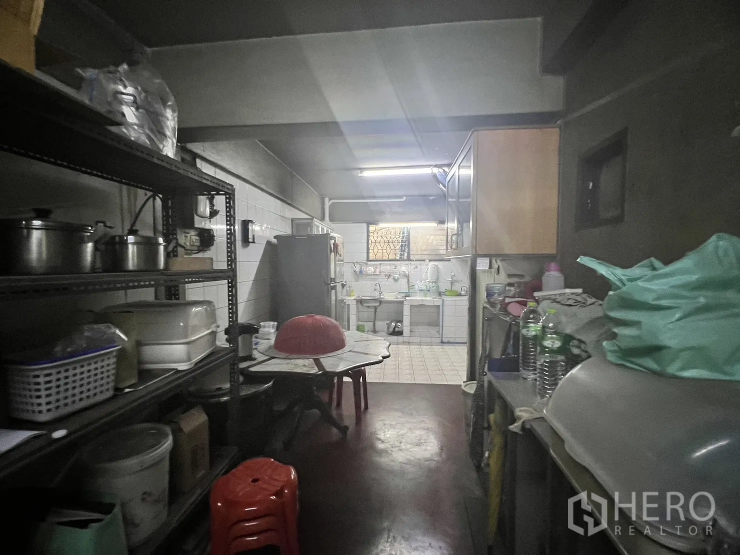 Retail Space for rent in Watthana, Bangkok - Back-of-house prep area with metal shelving, fridge and a tiled sink under fluorescent lighting.
