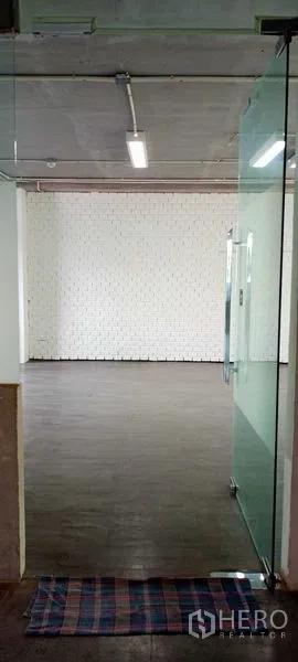 办公空间 出租在Khlong Toei, Bangkok - 玻璃门入口通向空置办公室，白砖特色墙、深色地板与线性顶灯。