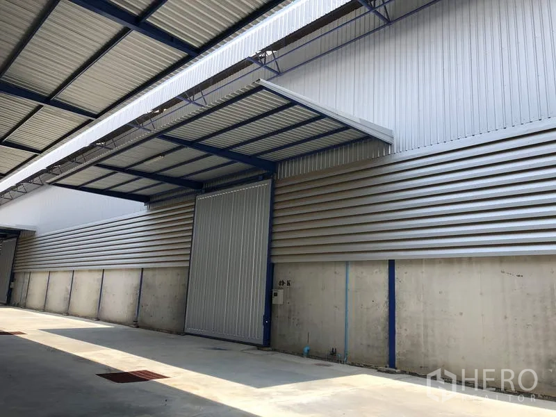 Factory for rent in Lat Lum Kaeo, Pathum Thani - Sliding metal warehouse door with an awning and solid concrete wall, ready for loading.