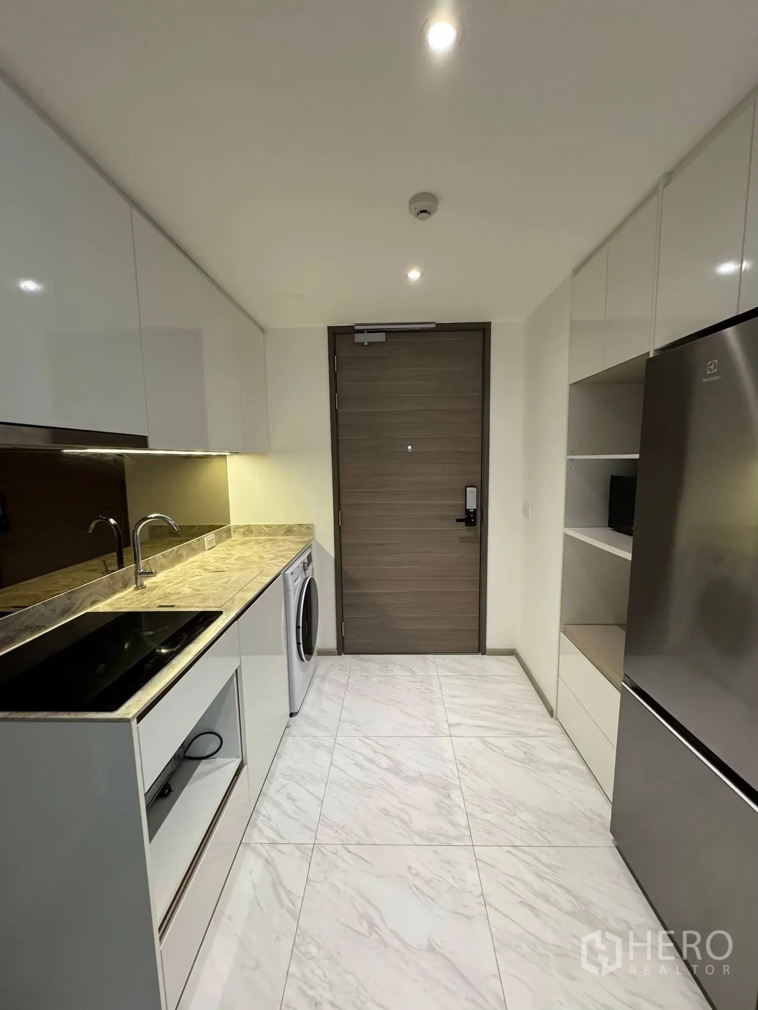 公寓 for rent in Khlong Toei, Bangkok - 长廊式厨房配石纹台面、电炉、洗衣机与大冰箱，柜体光亮整洁。