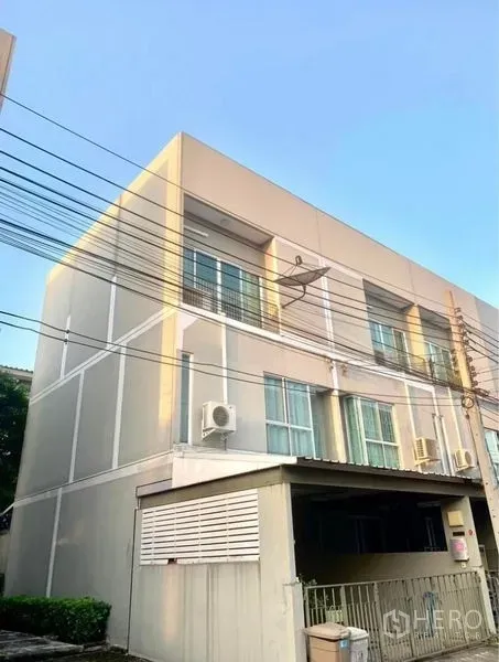 Townhouse for rent in Suan Luang, Bangkok - Three-storey townhouse exterior in Suan Luang, Bangkok with carport and large windows under clear sky.