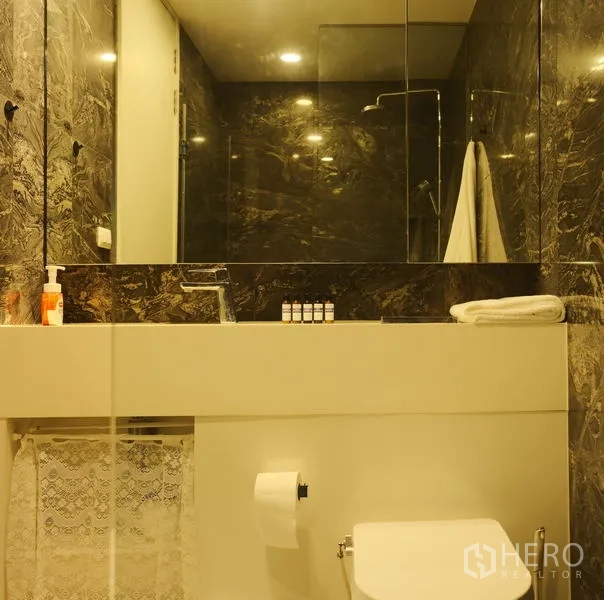 Condominium for rent in Bang Rak, Bangkok - Bathroom with large mirror, vanity, toilet and dark stone tiles.