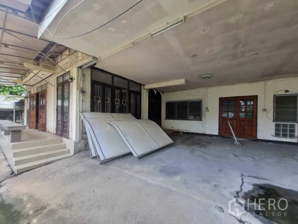 Detached House for rent or sale in Watthana, Bangkok - Covered carport and shaded terrace beside the house with multiple wooden doors.