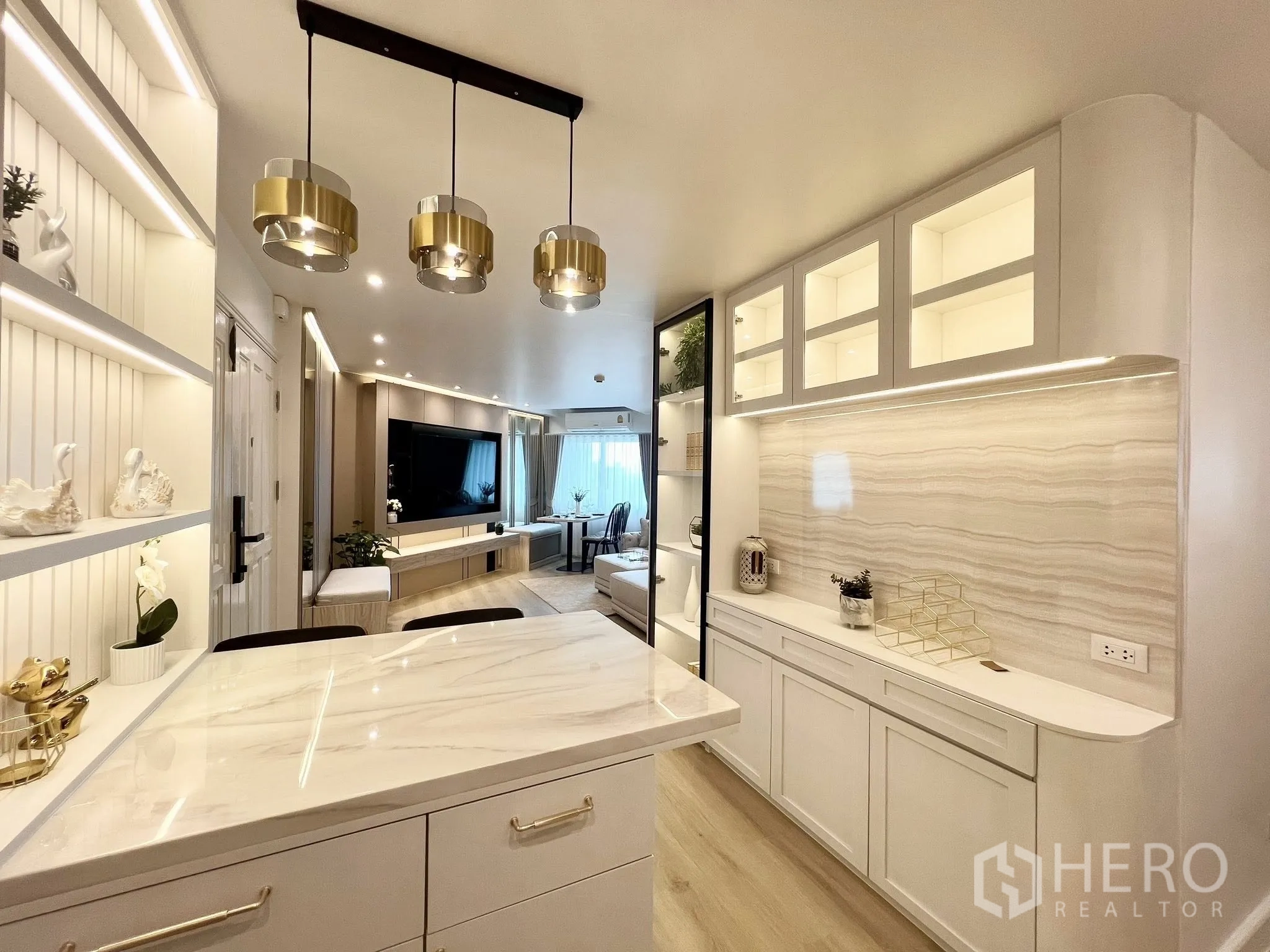 คอนโด for rent or sale in Yan Nawa, Bangkok - มุมครัวมองสู่ห้องนั่งเล่น พร้อมไอส์แลนด์หินอ่อน โคมแขวนสีทอง และชั้นโชว์ไฟในตัว