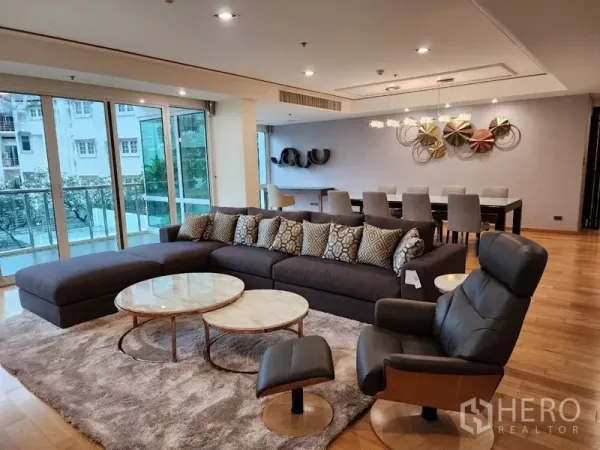 Condominium for rent in Khlong Toei, Bangkok - Spacious living room of luxury Khlong Toei condo with L‑shaped sofa, balcony and wood floors.