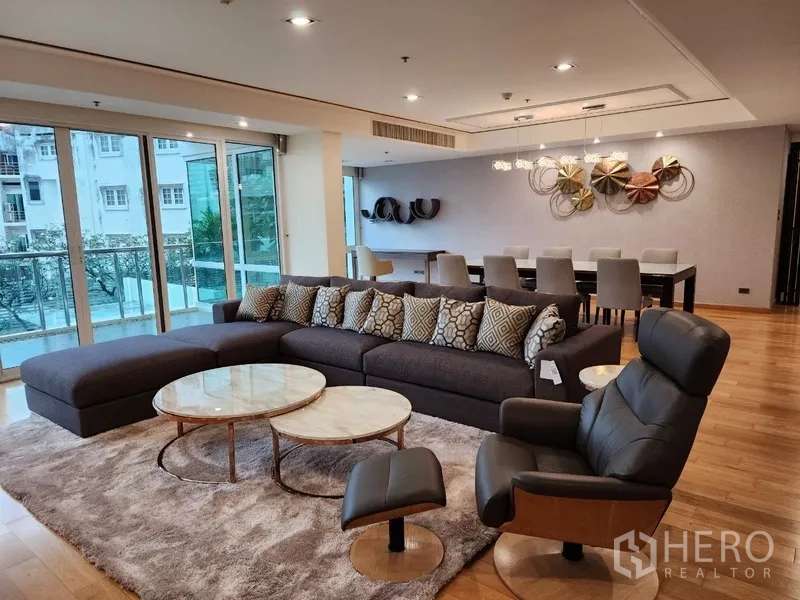Condominium for rent in Khlong Toei, Bangkok - Spacious living room of luxury Khlong Toei condo with L‑shaped sofa, balcony and wood floors.