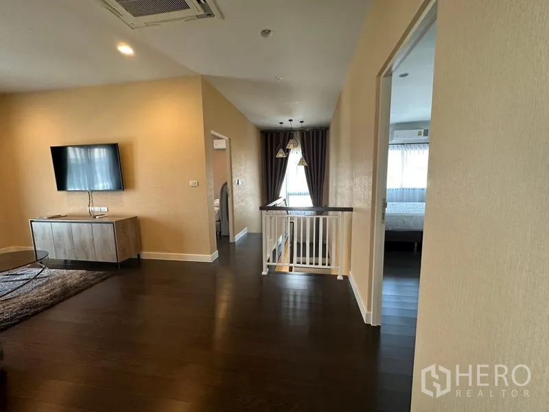 Detached House for rent or sale in Lam Luk Ka, Pathum Thani - Upstairs family lounge with TV, wood flooring and railing leading to bedrooms.