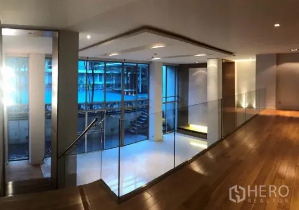 Condominium for sale in Khlong Toei, Bangkok - Modern corridor with wood floors and glass railing overlooking the courtyard pool at Ficus Lane condo in Phra Khanong.
