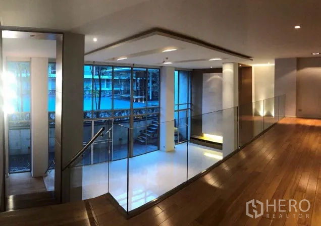 Condominium for sale in Khlong Toei, Bangkok - Modern corridor with wood floors and glass railing overlooking the courtyard pool at Ficus Lane condo in Phra Khanong.