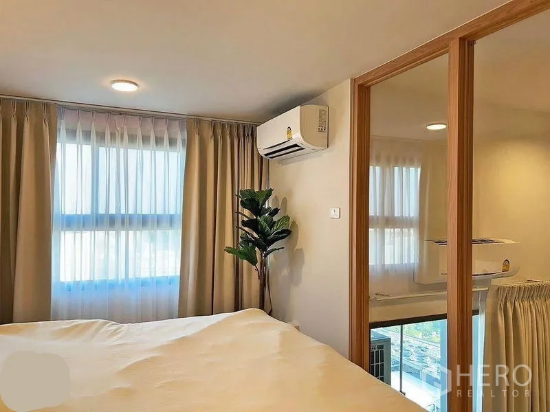 Condominium for rent in Huai Khwang, Bangkok - Mezzanine bedroom corner with sliding glass divider, window drapes, air conditioner and indoor plant.