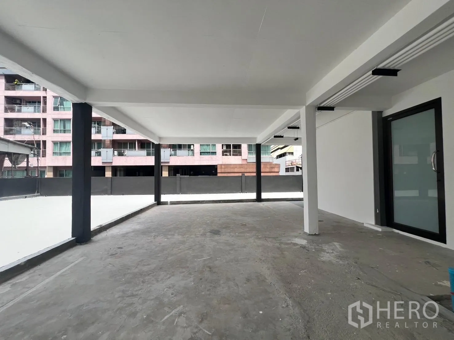 零售空间 for rent in Bang Rak, Bangkok - 开放式遮蔽零售区，混凝土地面、白色天花、黑色立柱与玻璃门，可见周边建筑景观。