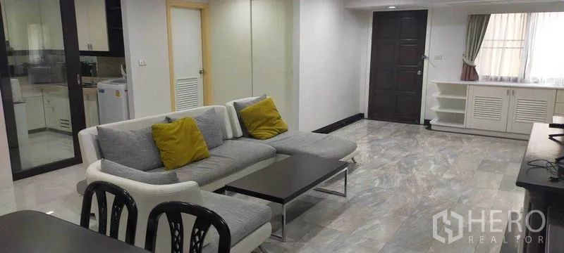 Condominium for rent in Watthana, Bangkok - Spacious living room with gray sectional sofa, marble floors, and built-in cabinetry.