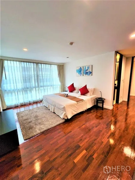 Condominium for rent in Bang Rak, Bangkok - Large bedroom with area rug, bedside table, and a wide window.