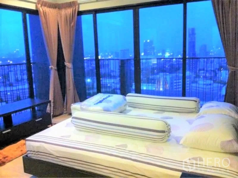 Condominium for rent in Watthana, Bangkok - Corner master bedroom featuring panoramic floor‑to‑ceiling windows with curtains and expansive city view.