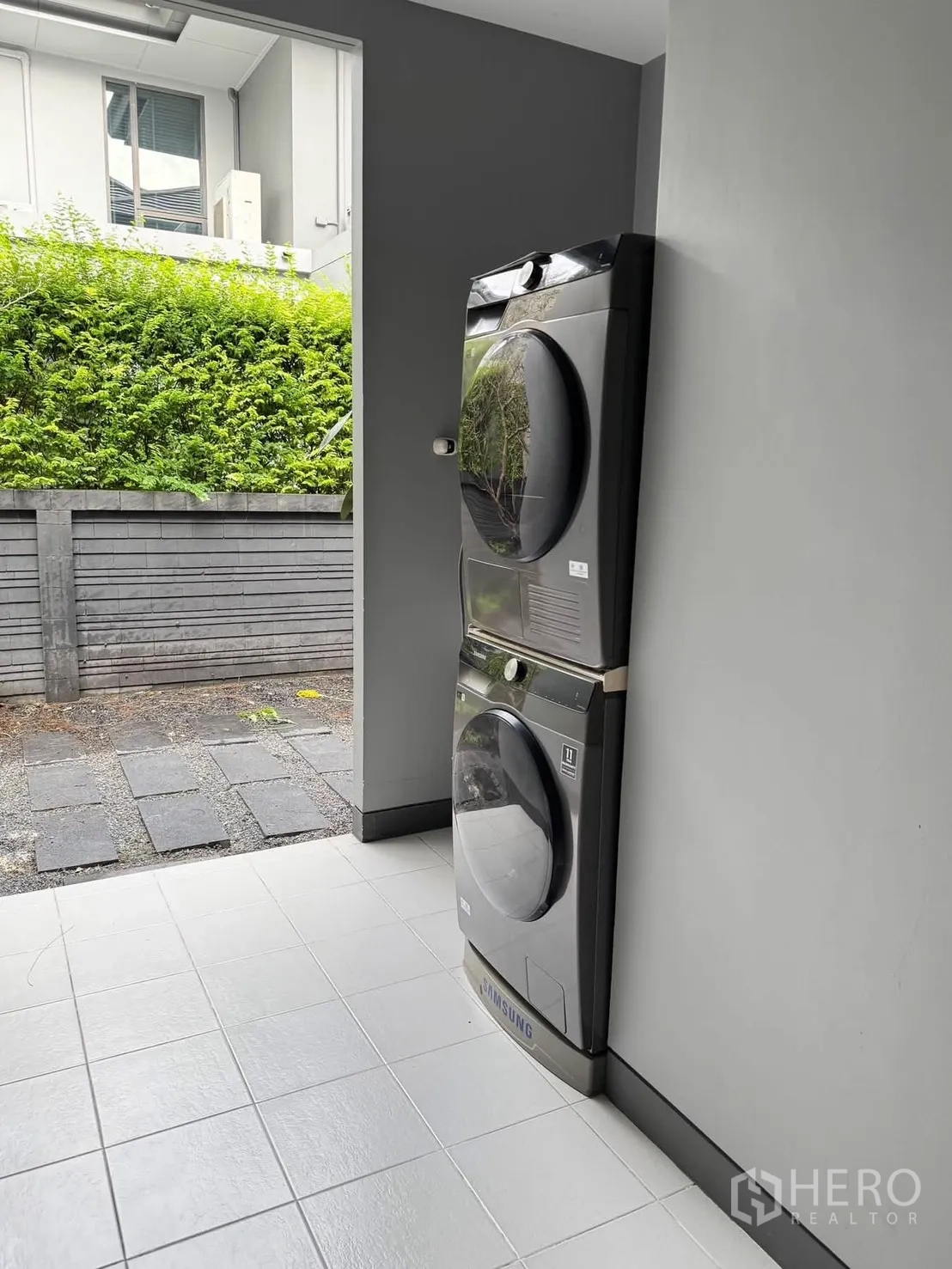 Detached House for rent in Bang Kapi, Bangkok - Covered laundry area with stacked washer and dryer next to a hedge.