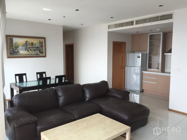 公寓 出租或出售在Khlong Toei, Bangkok - 客餐一体的起居室，深色皮沙发、玻璃餐桌及带不锈钢冰箱的紧凑厨房。