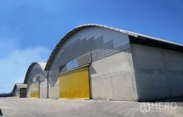 คลังสินค้า ให้เช่าในPhra Pradaeng, Samut Prakan - อาคารโกดังหลังคาโค้งผนังคอนกรีต ประตูบานเลื่อนสีเหลือง ใต้ท้องฟ้าแจ่มใส
