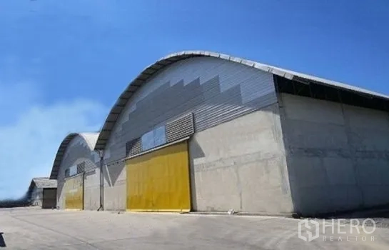 คลังสินค้า ให้เช่าในPhra Pradaeng, Samut Prakan - อาคารโกดังหลังคาโค้งผนังคอนกรีต ประตูบานเลื่อนสีเหลือง ใต้ท้องฟ้าแจ่มใส