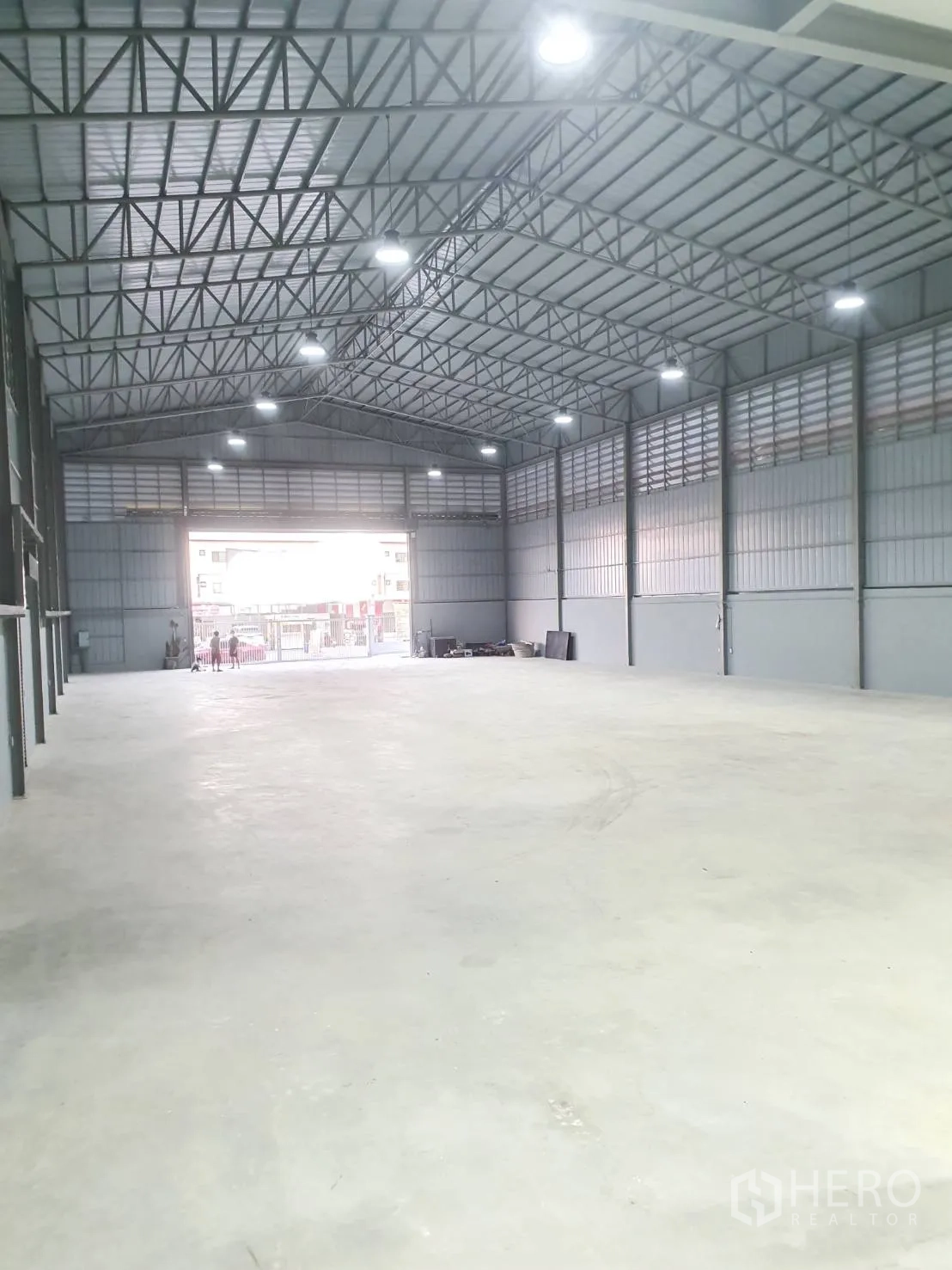 Warehouse for rent in Sai Mai, Bangkok - Long central warehouse aisle under a gabled steel roof with high-bay lights and open shutter.