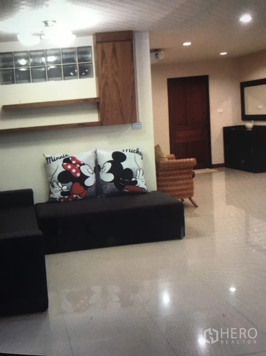Condominium for rent in Bang Rak, Bangkok - Living space with a black sofa, playful Mickey and Minnie cushions, shelving and glossy tile floors.
