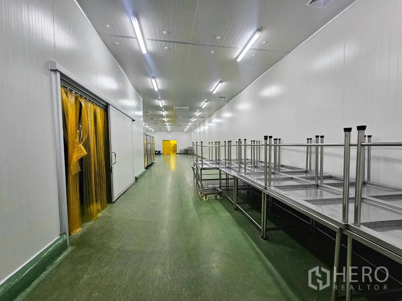 โรงงาน for rent in Mueang Samut Sakhon, Samut Sakhon - ทางเดินพื้นเขียวพร้อมโต๊ะสเตนเลสและม่านพีวีซีสีเหลือง