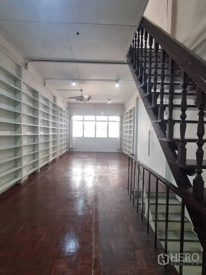 Shophouse for rent in Phra Khanong, Bangkok - Long room with twin rows of built-in white shelves, parquet flooring, and a stairway.