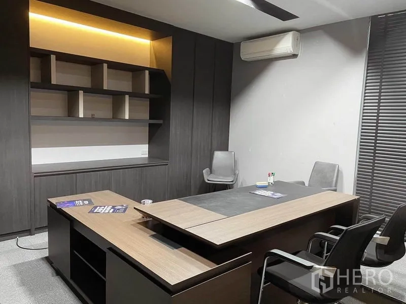Office Space for rent in Bang Na, Bangkok - Executive office with wood desk, built‑in shelving, air conditioner and blackout blinds.